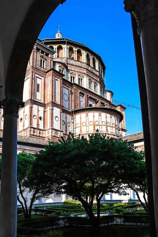 Wewnętrzny krużganek z widokiem na kościół Santa Maria delle Grazie w Mediolanie, miejsce znane z fresku „Ostatnia Wieczerza” Leonarda da Vinci.