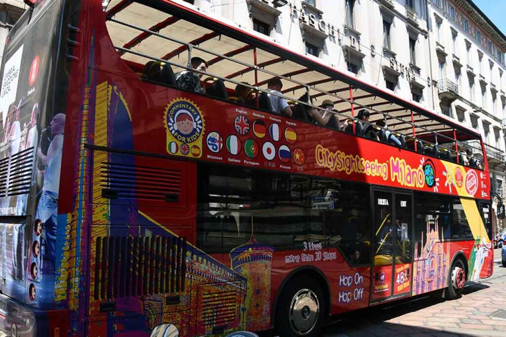 Autobus City Sightseeing w Mediolanie, zapewniający wygodny i wciągający sposób na zwiedzanie miasta. Zdjęcie przedstawia kolorowy piętrowy autobus z pasażerami podziwiającymi widok z górnego pokładu. 