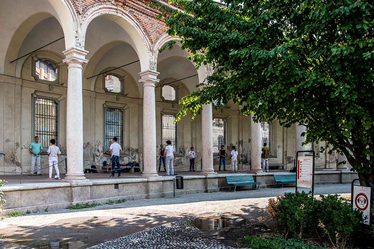 Ludzie ćwiczący Chi Gong pod portykiem Rotonda della Besana, cieszący się spokojną atmosferą i starożytnymi ćwiczeniami