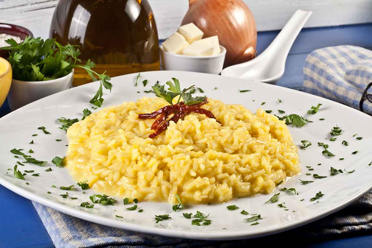 Risotto alla Milanese, tradycyjne danie z Mediolanu, przygotowywane z ryżu, szafranu i bulionu, charakteryzujące się kremową konsystencją i intensywnym kolorem.