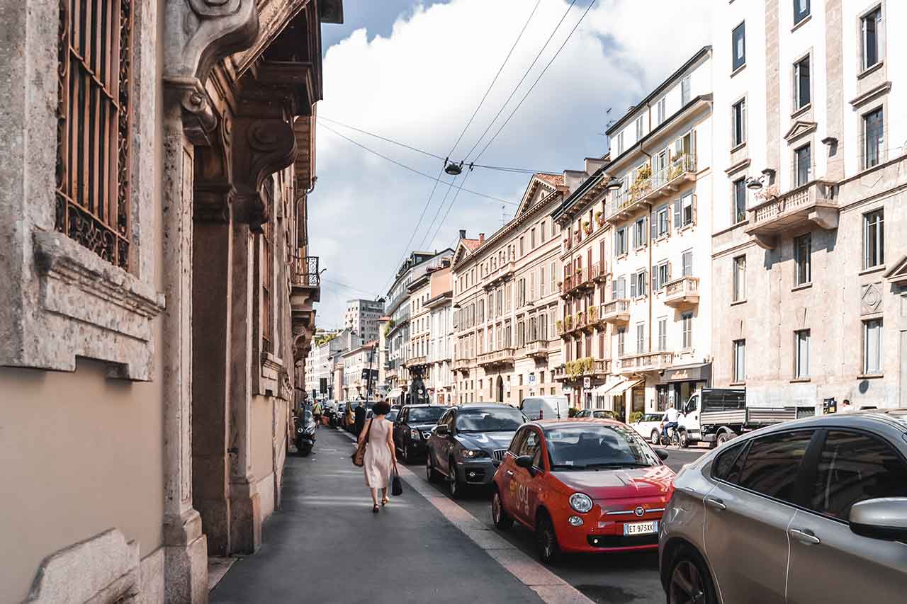 A picturesque view of Corso Venezia in Milan, Italy. The street presents a mix of historic buildings and elegant storefronts of luxury boutiques.
