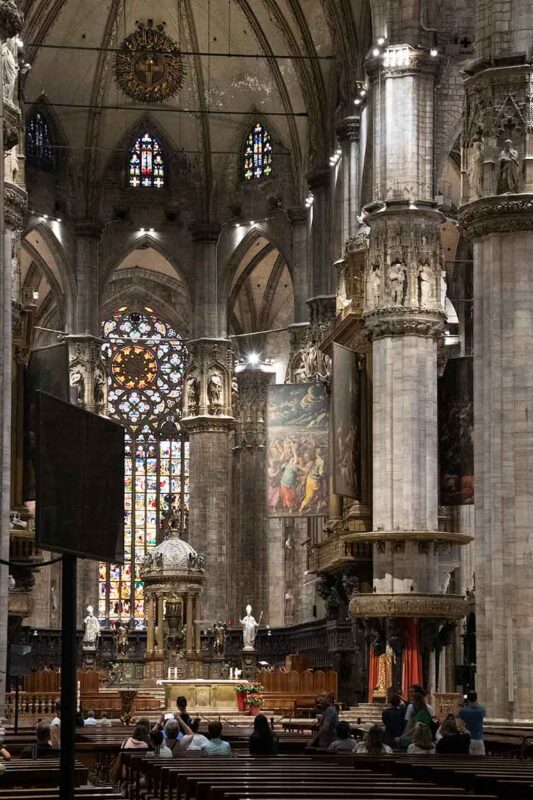 Wnętrze katedry Duomo w Mediolanie, ukazujące wspaniałą gotycką architekturę ze strzelistymi kolumnami i skomplikowanymi witrażami.
