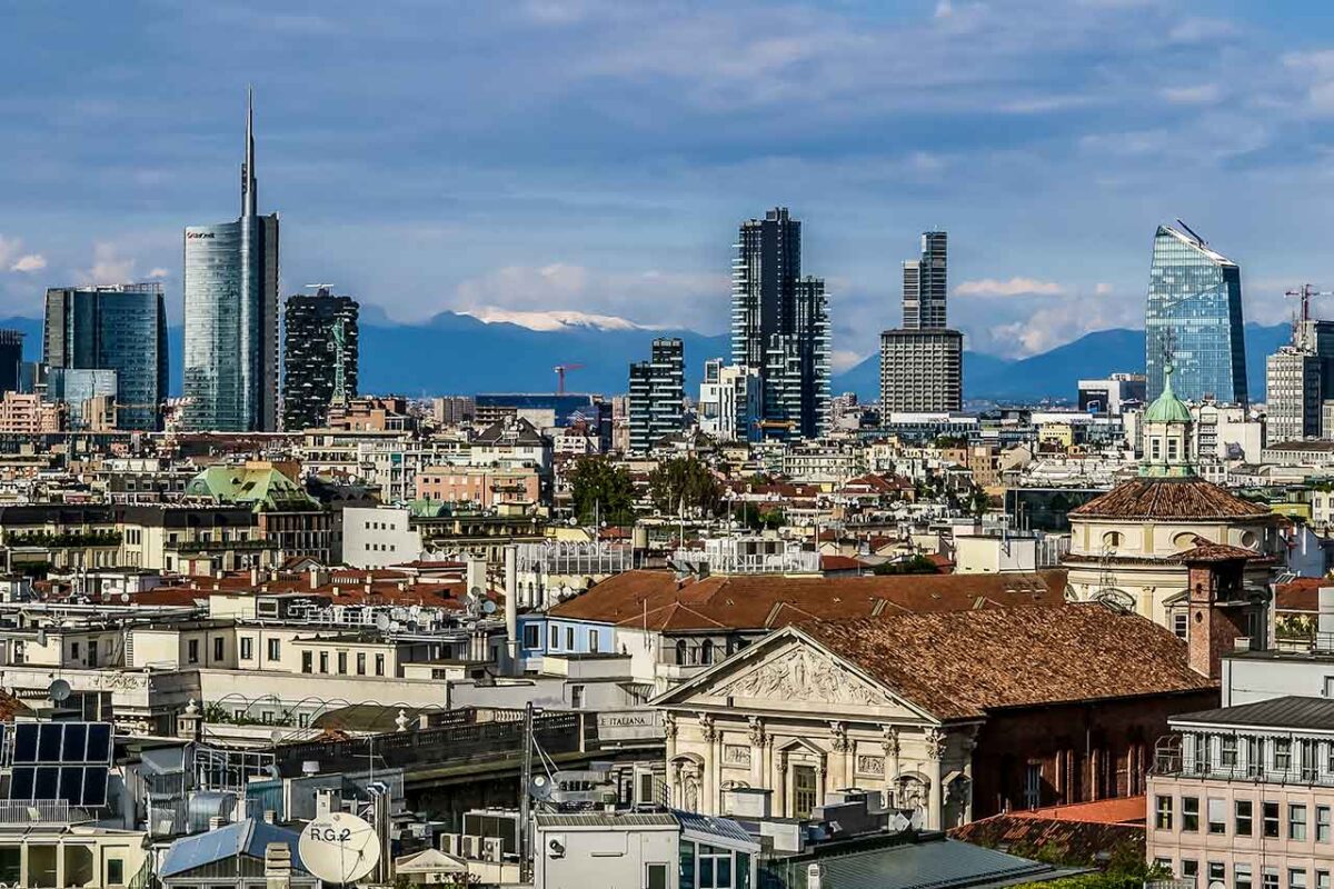 Panorama dachów Mediolanu, ukazująca zróżnicowaną architekturę miasta z widokiem na zabytkowe i nowoczesne budynki w tle.