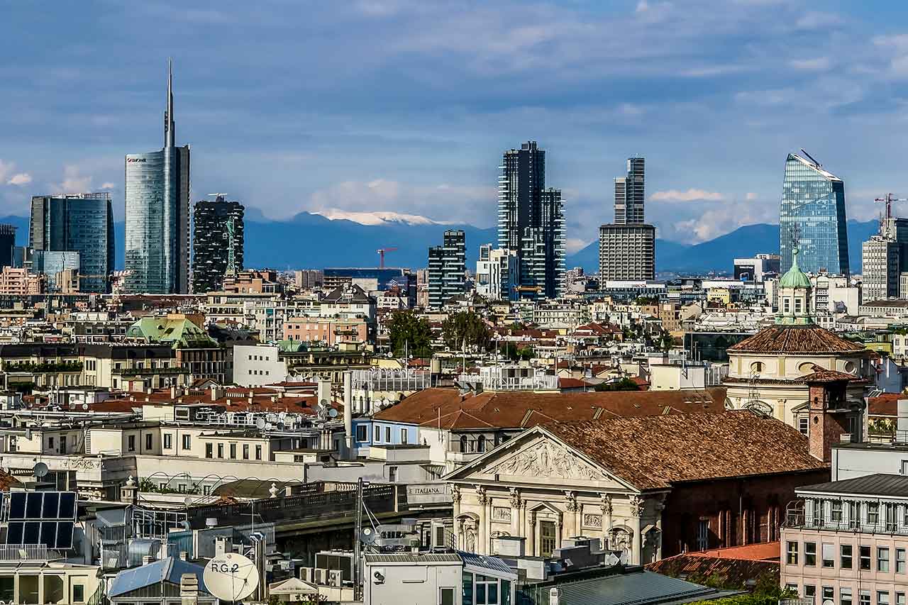 Panorama dachów Mediolanu, ukazująca zróżnicowaną architekturę miasta z widokiem na zabytkowe i nowoczesne budynki w tle.
