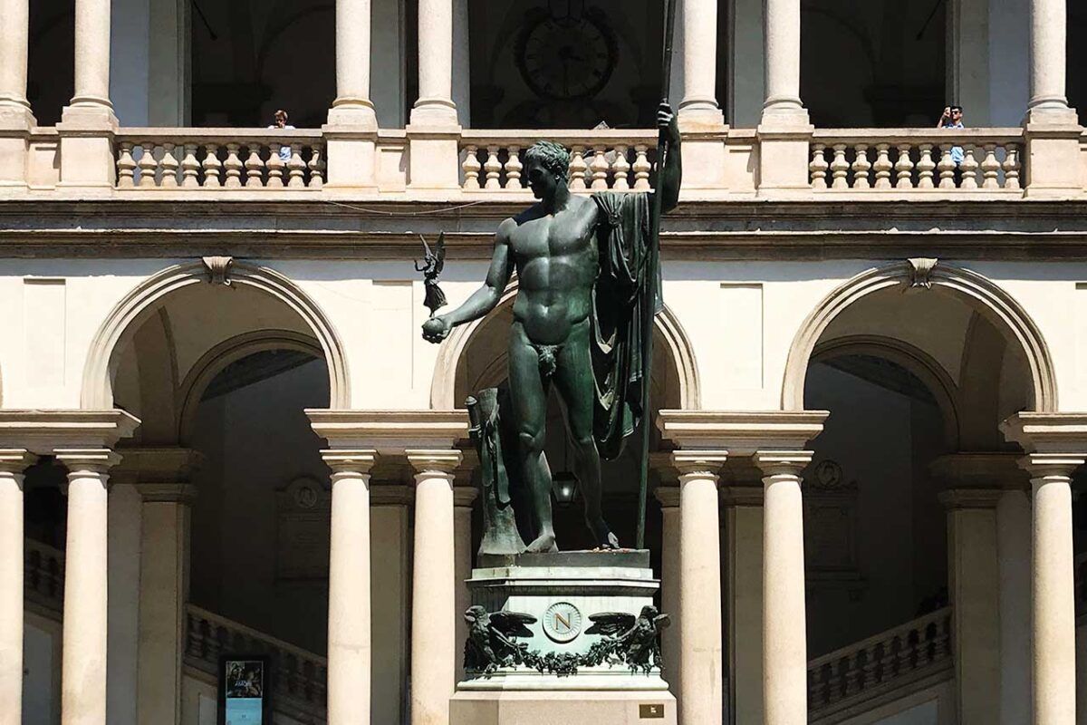 Pomnik na dziedzińcu Pinacoteca di Brera w Mediolanie, otoczony zabytkową architekturą i stanowiący centralny punkt wejścia do galerii sztuki.