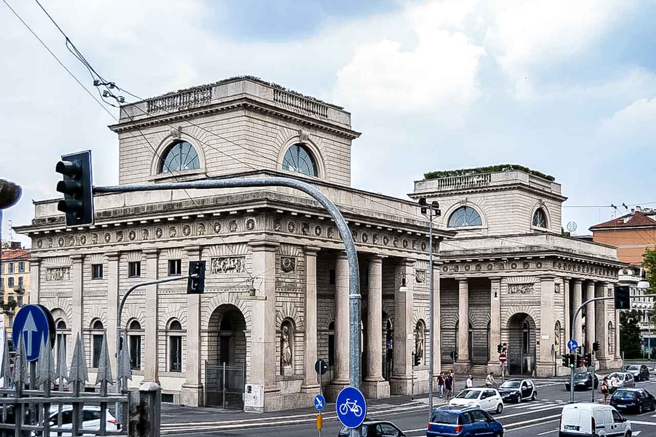 Porta Venezia w Mediolanie, historyczna brama miejska i punkt orientacyjny, otoczona eleganckimi budynkami i zielenią, w pobliżu głównej ulicy handlowej Corso Buenos Aires.