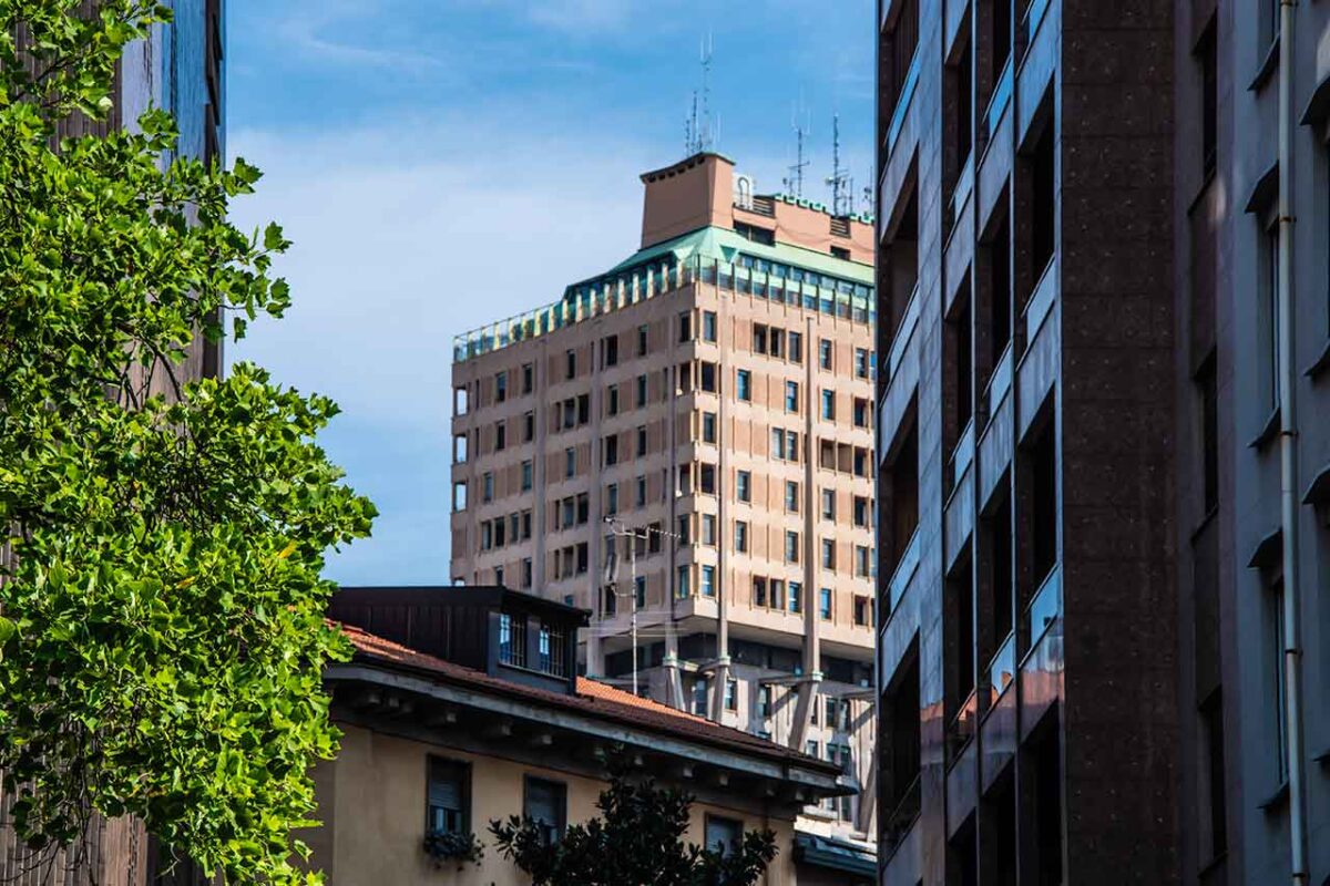Górna część wieżowca Torre Velasca w Mediolanie, widziana spomiędzy okolicznych budynków, charakterystyczna ikona architektury modernistycznej miasta.