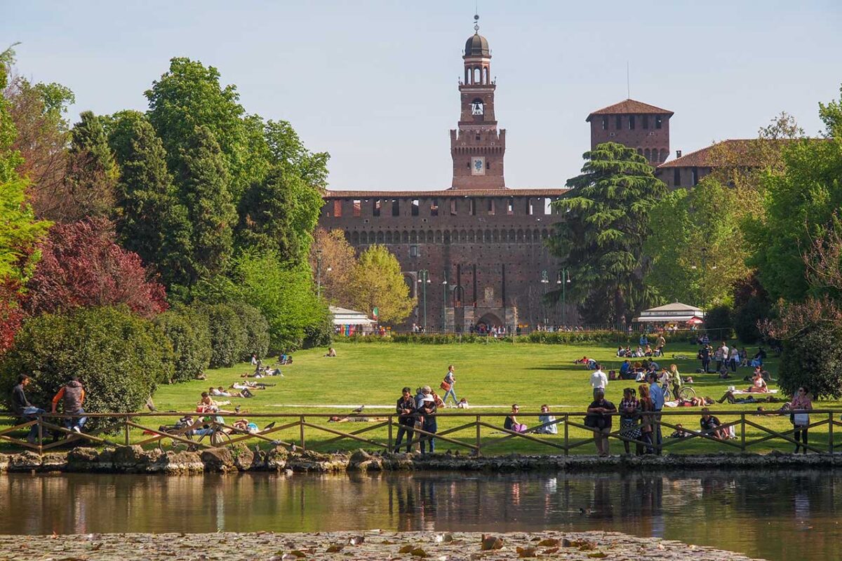 Ludzie odpoczywający na trawie w Parco Sempione w Mediolanie w słoneczny, wiosenny dzień, w tle Zamek Sforzów